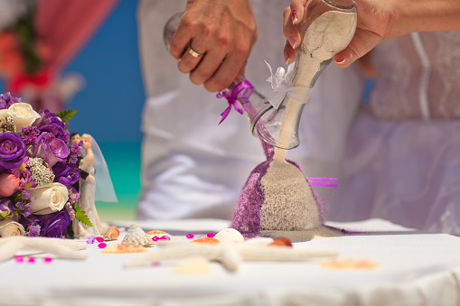 The bride and groom pour sand in a colorful bowl. Ceremony colored sand.