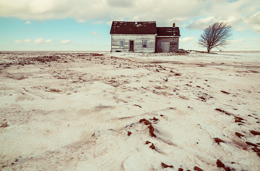An abandoned farm house sits alone in a windswept field on a cold February afternoon.