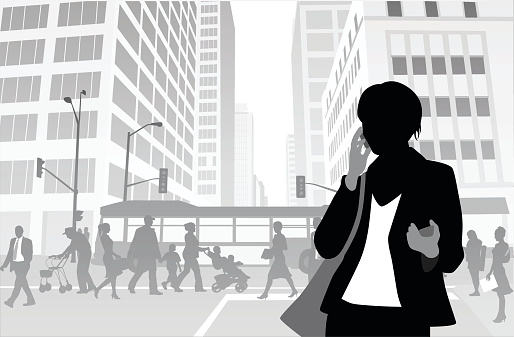 A vector silhouette illustration of a young woman talking on her cell phone while holding a second cell phone in the other hand.  She stands in a crowded city street with commutes crossing a side walk, a bus traveling through an intersection, and tall office buildings.