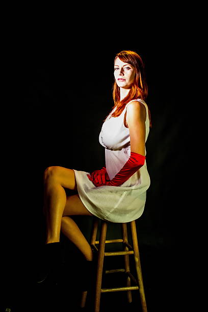 very attractive young blonde girl / woman in her emerald dress sitting on a white chair with her legs x-shaped
