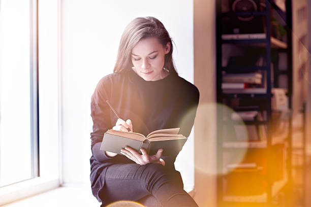 Young brunette woman with a book in a public library. Young brunette woman with a book in a public library. Sitting near window teen wishing stock pictures, royalty-free photos & images