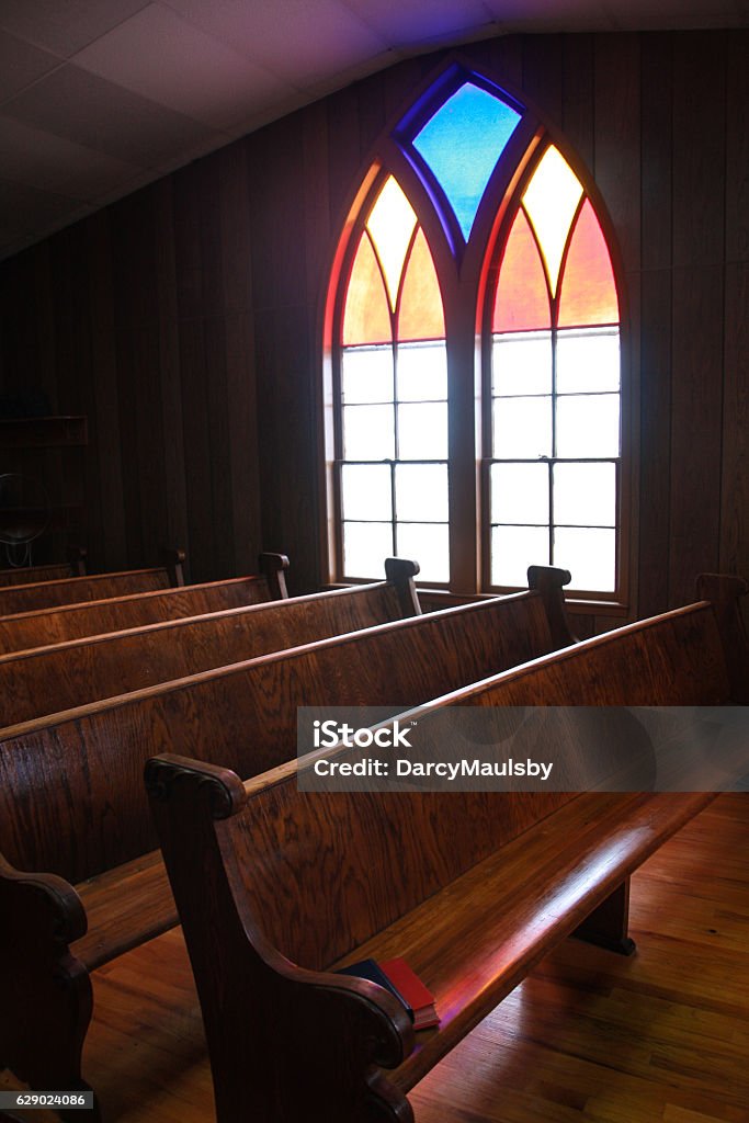 Iowa Country Church Stained Glass Window This arched, stained glass window casts a soft glow on the wooden pews in this central Iowa country church.  Church Stock Photo