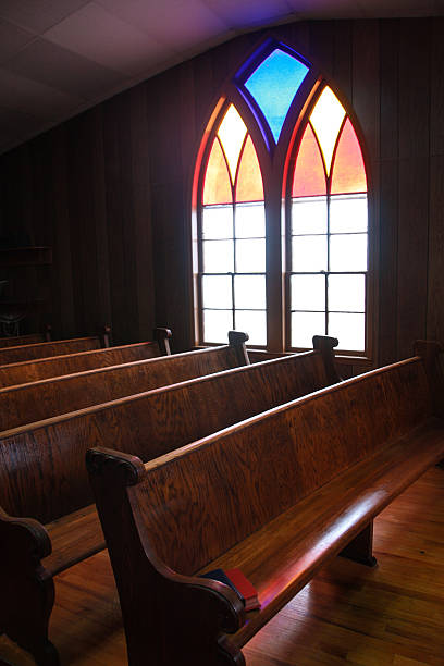 Iowa Country Church Stained Glass Window This arched, stained glass window casts a soft glow on the wooden pews in this central Iowa country church.  pew stock pictures, royalty-free photos & images