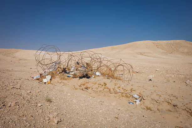 Rusting barbed wire in the desert of Kuwait, covered in trash blown in by the wind. Remnant of the war.