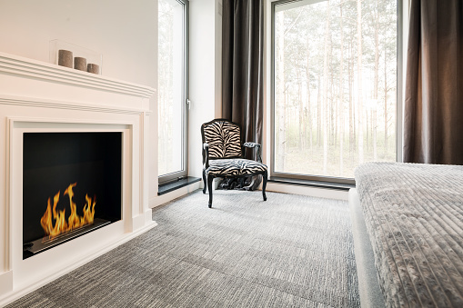 Grey master bedroom with elegant fireplace, chair, bed and panoramic window