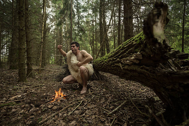 Caveman in animal skin kindles a fire in the forest