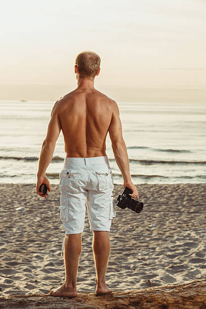 hombre delgado en pantalones cortos en una playa con cámara - men refreshment male summer fotografías e imágenes de stock