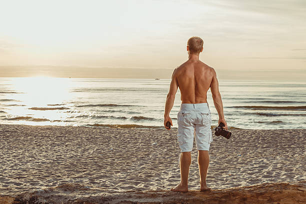 hombre delgado en pantalones cortos en una playa con cámara - men refreshment male summer fotografías e imágenes de stock