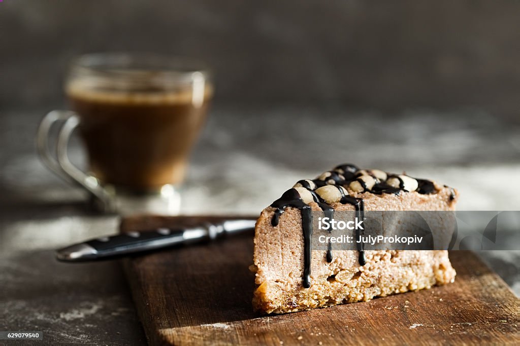 Vegan chocolate mousse cake and coffee on a stone background Healthy raw chocolate mousse cake  with cashew nuts, hazelnuts and dark chocolate glaze topping and coffee on a wooden and grey stone background. Vegan sugar, gluten, dairy free dessert. Dark food photography. Horizontal Antioxidant Stock Photo