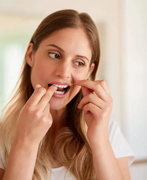 Cropped shot of a young woman flossing her teeth at home