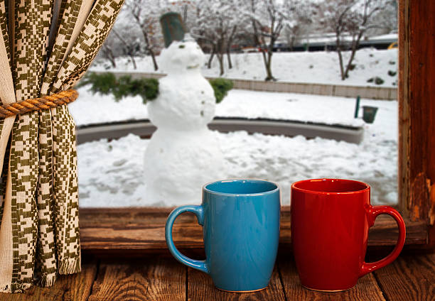 Cups of hot tea  on vintage windowsill against snowman from outside