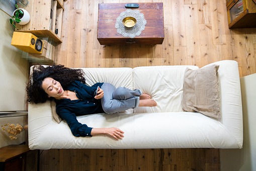 Mature woman looking at a smartphone while lying on a sofa at home in her apartment