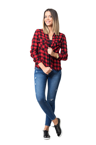 Beautiful happy woman posing white holding collar of red plaid shirt in jeans. Full body length standing portrait isolated over white background.