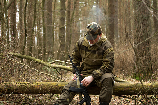 a military man in the woods with a Kalashnikov assault rifle, autumn forest with no leaves, green form, No face.