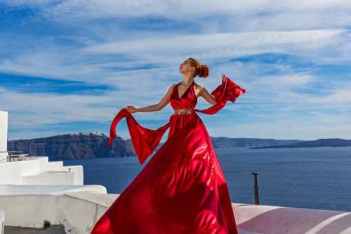 Beautiful young woman in red dress on the background of the architecture in Santorini
