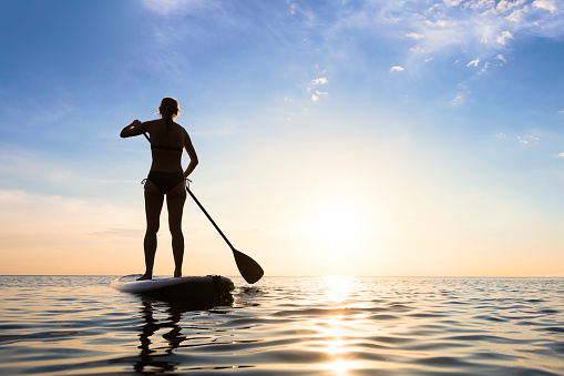 Girl stand up paddle boarding (sup) on quiet sea, sunset