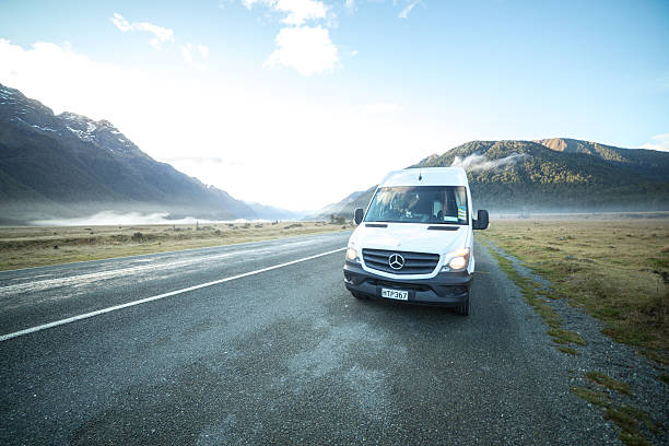 Fiordland national park, New Zealand - June 28, 2016: Camper-van driving on countryside road, mountains on the background.