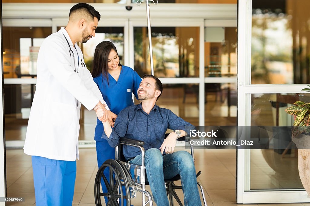 Patient leaving the hospital on a wheelchair Happy and recovered patient sitting on a wheelchair and saying goodbye to his doctor while leaving the hospital Hospital Stock Photo