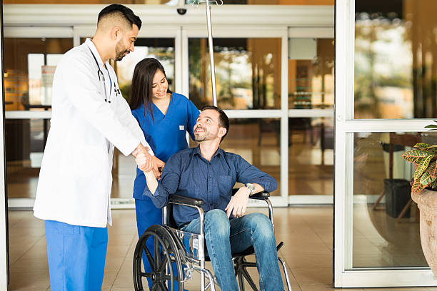 Patient leaving the hospital on a wheelchair Happy and recovered patient sitting on a wheelchair and saying goodbye to his doctor while leaving the hospital goodbye stock pictures, royalty-free photos & images
