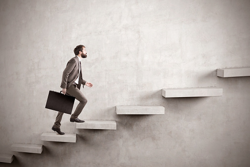 Side view of a man climbing the stairs built in a blank concrete wall. Concept of success and achieving your goal. Mock up