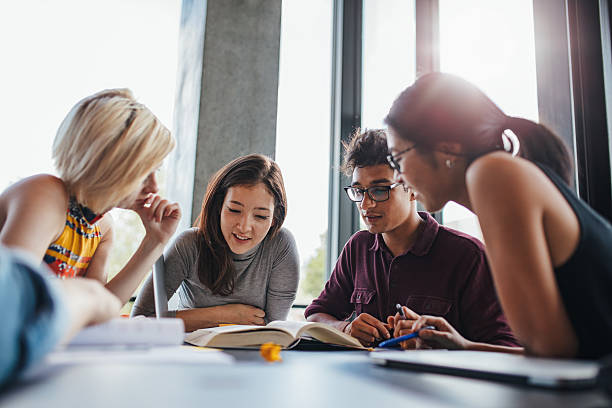 groupe de jeunes assis à table à lire des livres - étudiant photos et images de collection