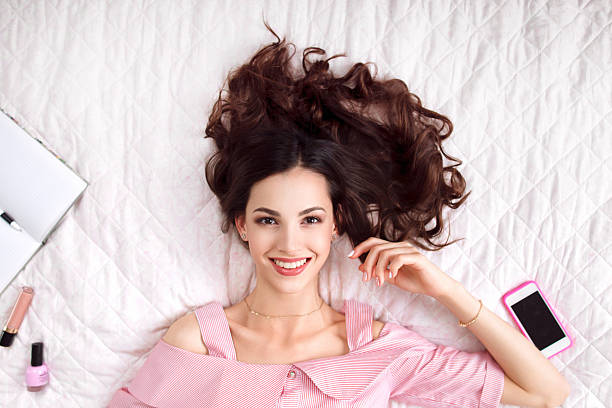 Beautiful woman lying on bed top view Beautiful woman lying on bed top view. Happy brunette in pink with healthy perfect hair smiling at camera. Beauty, joy, health care, fashion concept pink bed stock pictures, royalty-free photos & images