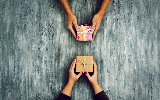 high-angle shot of a young caucasian woman and a young caucasian man exchanging gifts on a rustic wooden table, with some negative spaces around them