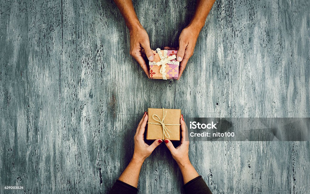 woman and man exchanging gifts high-angle shot of a young caucasian woman and a young caucasian man exchanging gifts on a rustic wooden table, with some negative spaces around them Gift Stock Photo