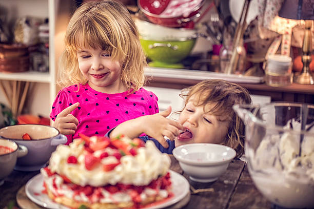 Cule Kids Eating Berry Pavlova Cake with Strawberries and Raspberries Cute little kids eating delicious Berry Pavlova Cake with fresh strawberries, raspberries, mint leaves and whipped cream. pavlova stock pictures, royalty-free photos & images