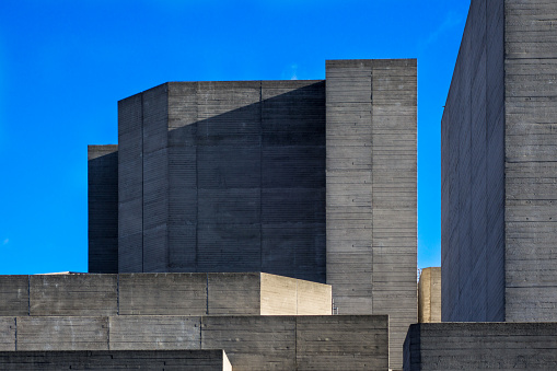 Parts of the brutalist architecture facade of the National Theatre in London against a blue sky