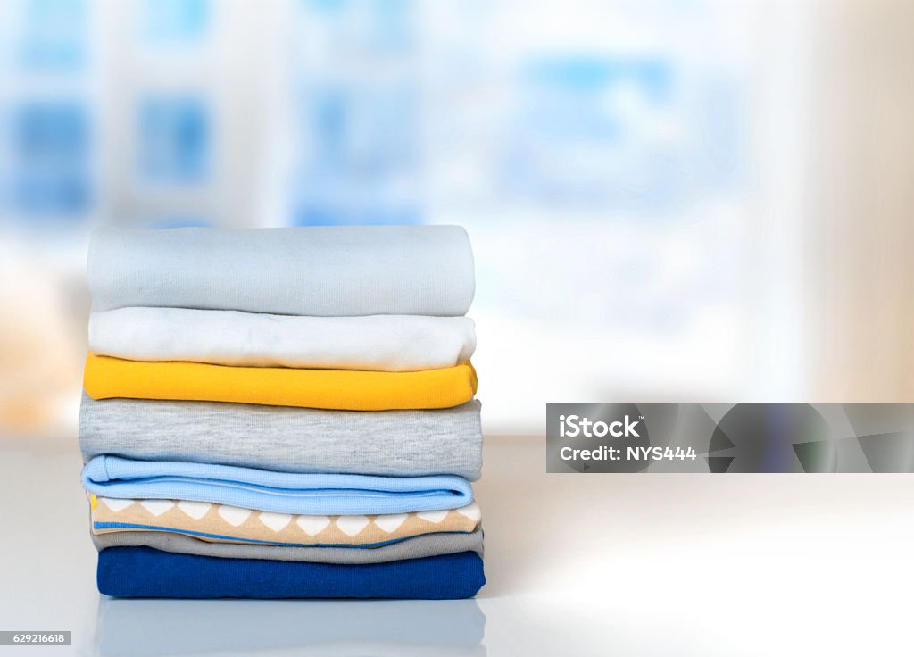 Stack cotton folded clothes on table indoors empty space. Cotton stack of colorful folded clothes on white table indoors empty space background.Household concept.Clean laundry pile. Clothing Stock Photo