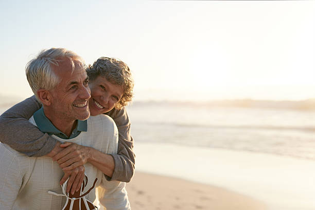 Senior couple having fun at the beach Portrait of happy mature man being embraced by his wife at the beach. Senior couple having fun at the sea shore. beach lifestyle stock pictures, royalty-free photos & images