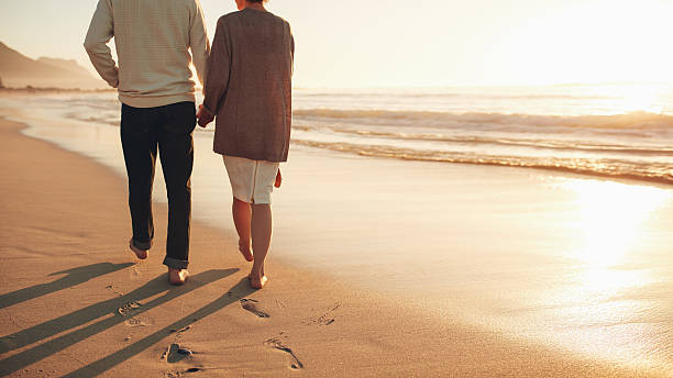 해변에서 걷는 손을 잡고 있는 시니어 커플 - men footprint beach sunset 뉴스 사진 이미지