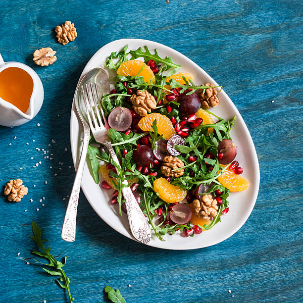 Delicious fruit salad. Grapes, tangerine, pomegranate and arugula fruit salad. On blue wooden background, top view. Flat lay