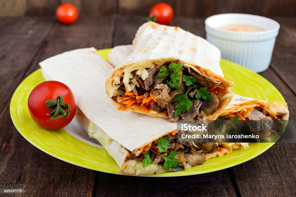 Shawarma sandwich - fresh roll of thin lavash (pita bread) Shawarma sandwich - fresh roll of thin lavash (pita bread) filled with grilled meat, mushrooms, cheese, cabbage, carrots, sauce, green. Traditional Eastern snack. On a dark wooden background. Beef Stock Photo