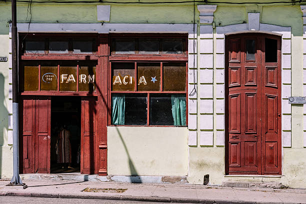 Havana, Cuba - October 13, 2016: Facades of Havana. Sunny side of one of the numerous wide boulevards in Old Havana center. Store front of local Pharmacy. Street level facade, part of the old colonial building with balconies on the second floor. Open front door of the store.