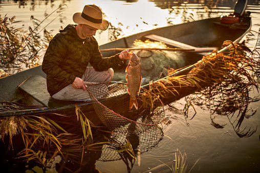 Portrait of a fisherman in his boat while holding net and a carp.