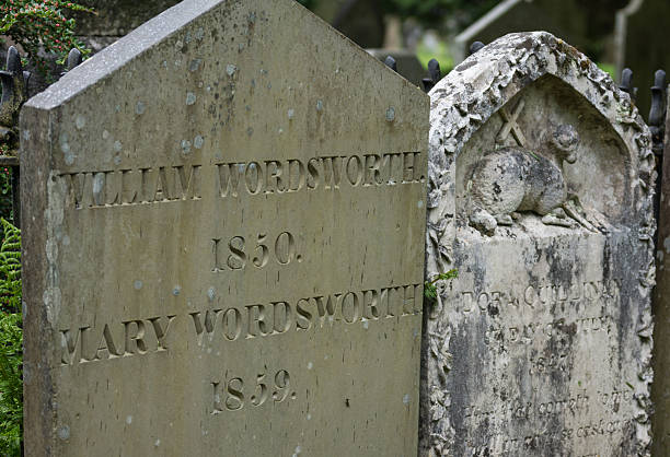Tombstone of William Wordsworth in Grasmere. Grasmere, England - May 30, 2012: In the cemetery of the Saint Oswald Church stands the gray old tombstone of the poet William Wordsworth and his wife Mary Hutchinson. Other tombstone with Agnus Dei. Green foliage. agnus dei stock pictures, royalty-free photos & images