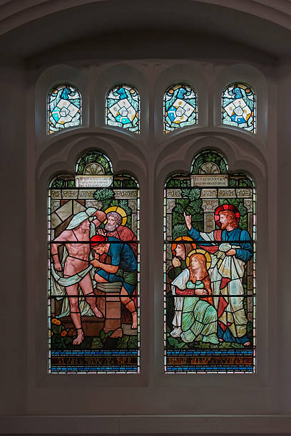 Stained glass window in Saint Oswald Church, Grasmere. Grasmere, England - May 30, 2012: Bright colored stained glass window at Saint Oswald Church shows scene out of Jesus life. Set in dark wall with smaller windows. Jesus tells to release a naked captive man. grasmere stock pictures, royalty-free photos & images