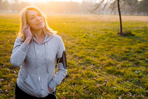 donna matura che fa jogging con la musica come motivazione per il runnng - jogging autumn young women women foto e immagini stock