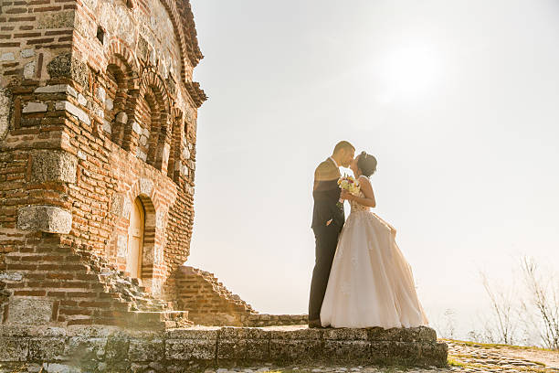 Happy newlyweds portait - strong handsome groom lifting bride in the air, husband holding wife in the air outdoors, church in the background, romance concept