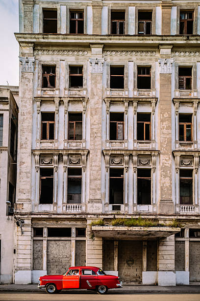 Havana, Сuba - October 11, 2016: Art Decco style abandoned building at the large boulevard in Center of Havana with in Chinatown area of the city. During last 50 years Havana had number of Asian (Chinese) immigrants as part of society. Especially during the happy days with Russians. After the break up of Eastern Block, and Russians leaving the Island, Chinese community has been on sharp decline. This area of the city  had seen better days. Red vintage American car  on the street. Driver inside.