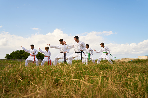 Hispanic men and children exercising in karate and traditional martial arts. Simulation of fight on the beach near the sea