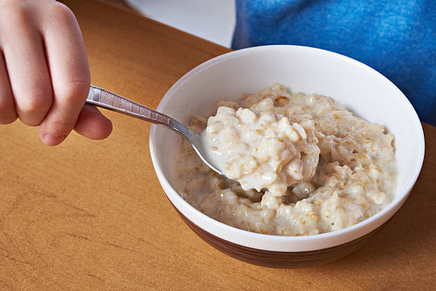 mano con cucchiaio di porridge a tavola primo piano - oatmeal porridge bowl spoon foto e immagini stock