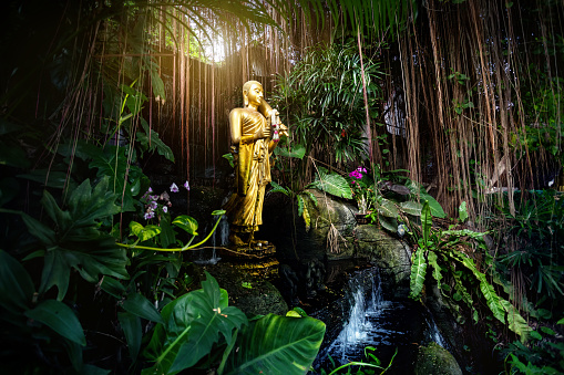 Golden Buddha statue in the tropical garden with waterfall in Wat Saket Golden Mountain Temple in Bangkok