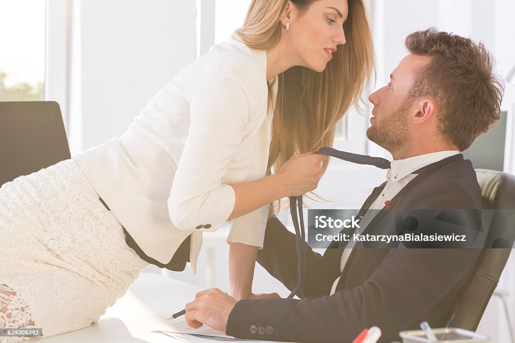 Woman  holding man's tie in the office Shot of a beautiful woman sitting on a desk in an office and holding elegant man's tie Office Stock Photo