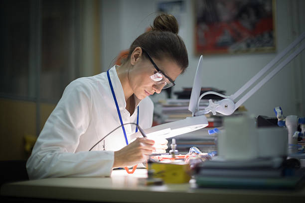 Female electrician using magnifying glass Mid adult female electrician working on drone at desk in industry, using magnifying glass robotic arm lab stock pictures, royalty-free photos & images