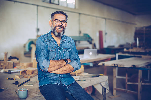 Confidence is the key to success. Carpenter in wood workshop. Mature man in casual clothing. Space is full of working tools and wooden planks. carpenter portrait stock pictures, royalty-free photos & images