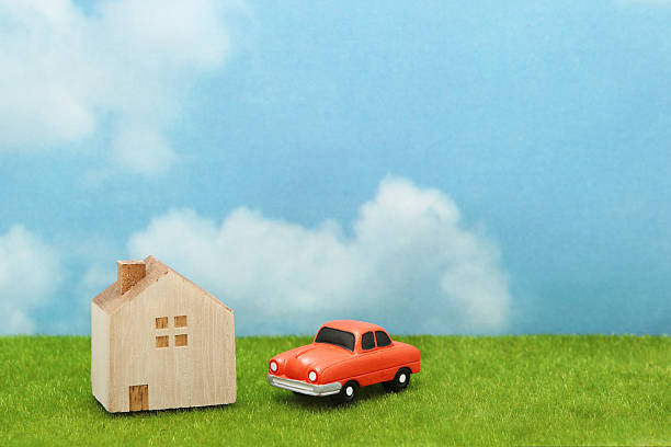 House and car on green grass over blue sky and clouds. My home and car concept.
