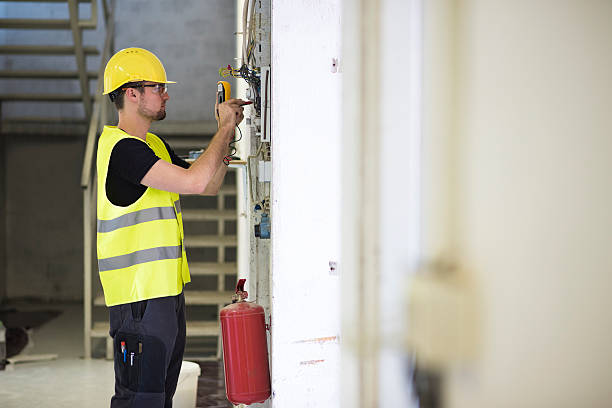 Is everything ok here? Electrician, wearing protective helmet, glasses and reflective vest testing voltage on construction site. electrician multimeter stock pictures, royalty-free photos & images